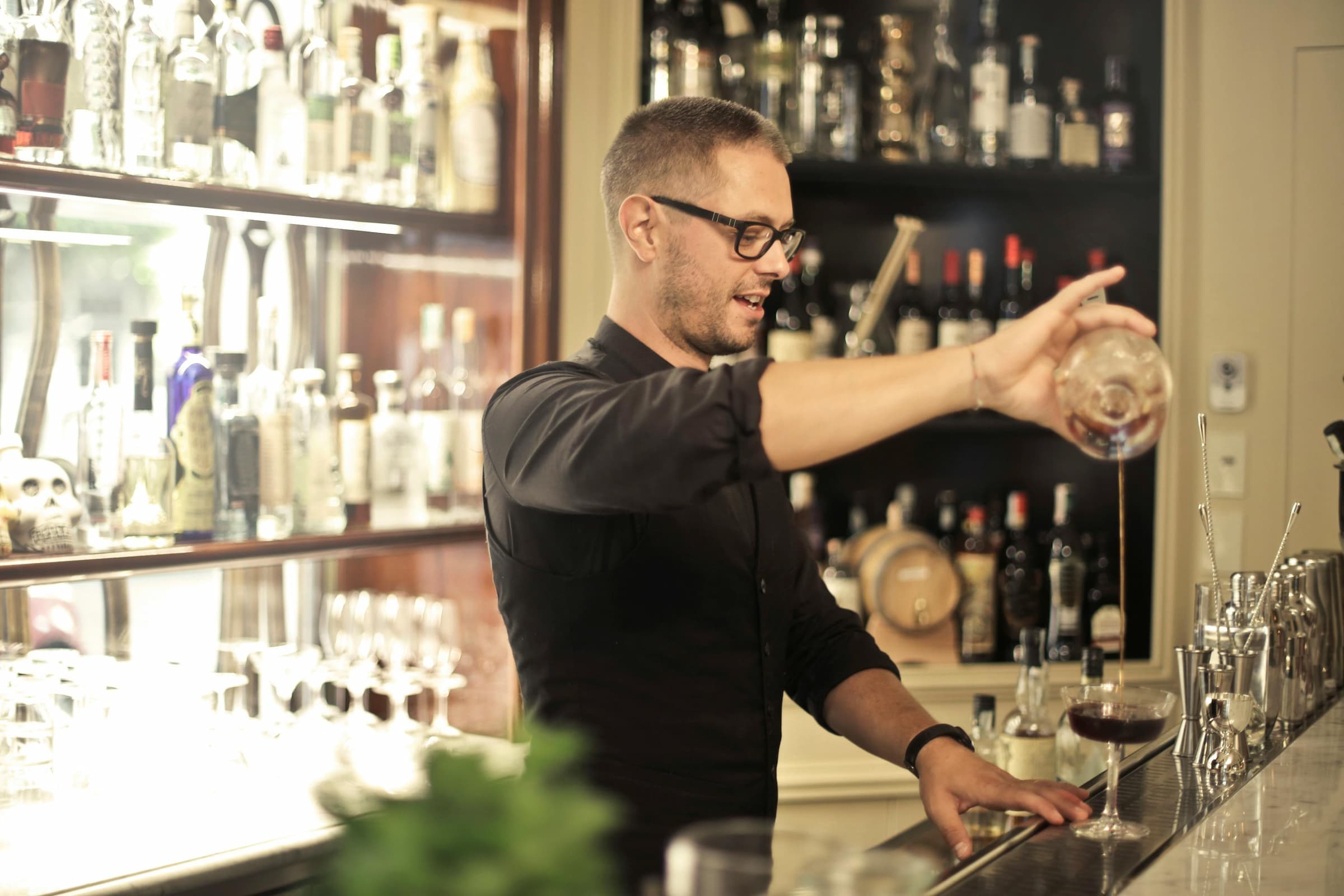 Bartender pouring a cocktail behind a stocked bar