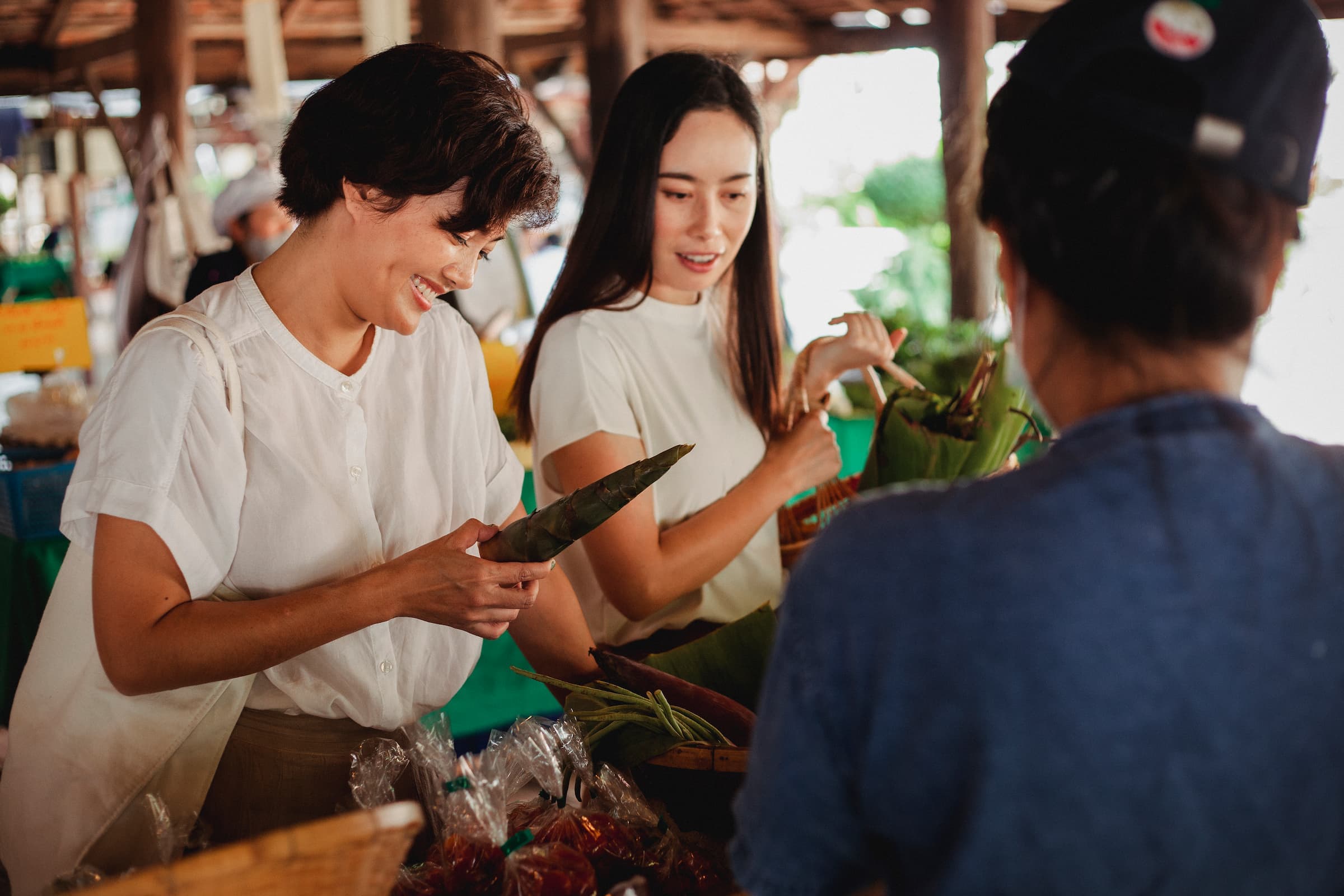 Market vendor at an outdoor farmers market booth handing a product to a customer
