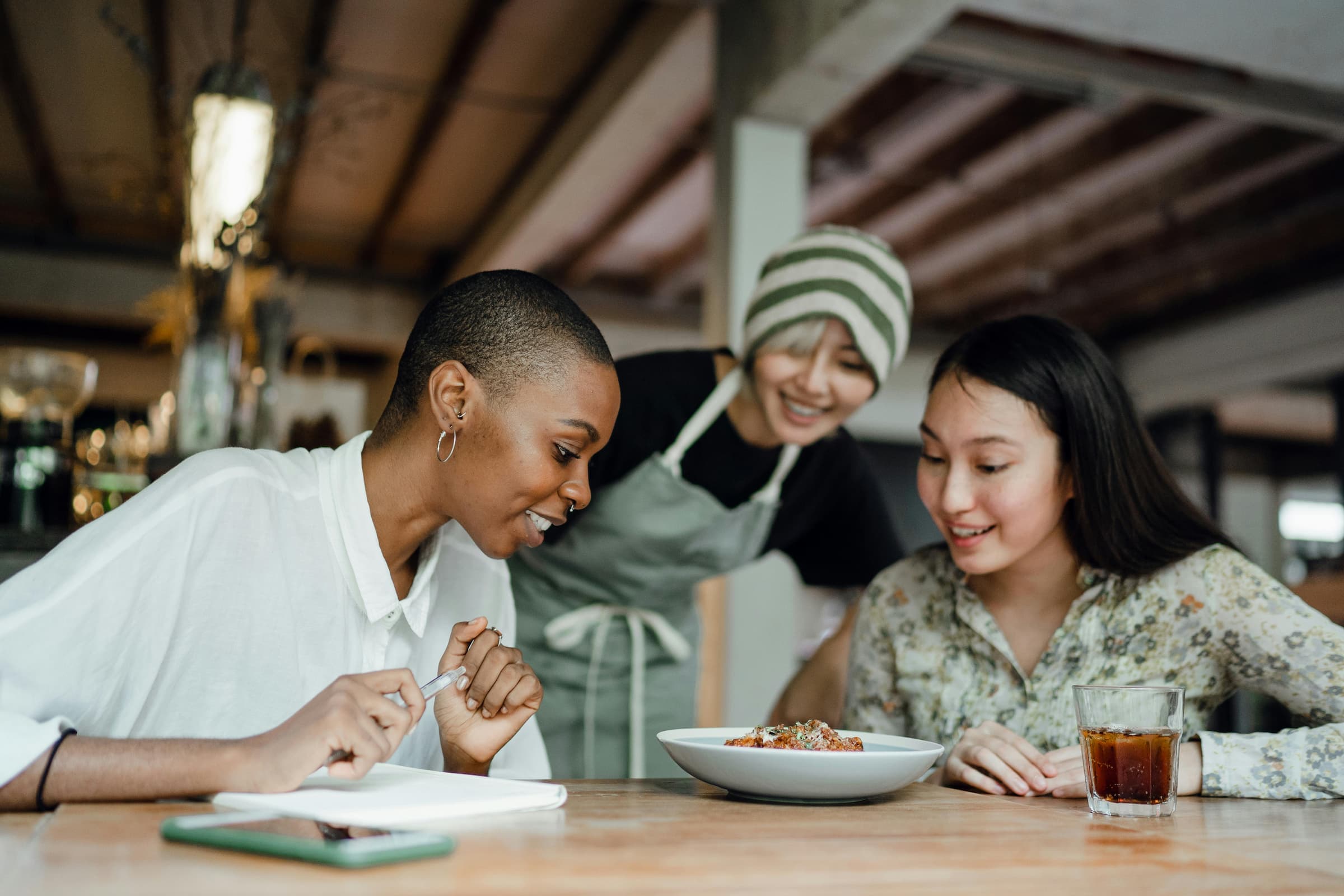 Happy restaurant server bringing food to a table of seated customers in a warm dining room